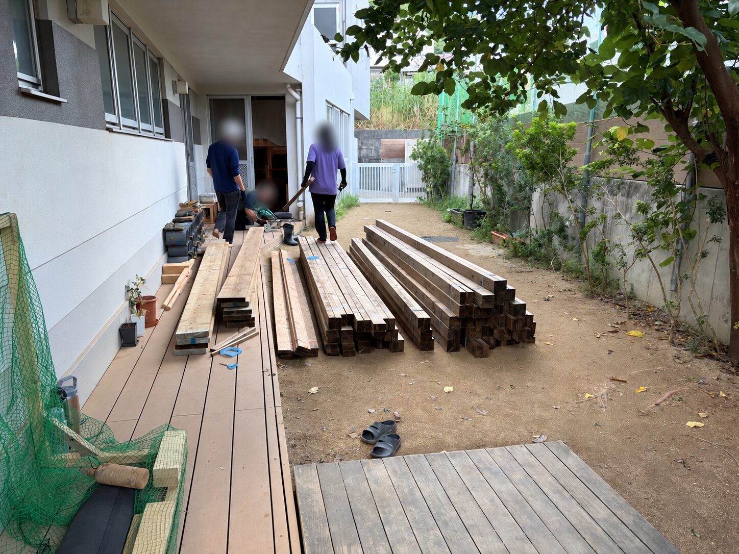 園舎の前に用意された木材と作業するおとな達